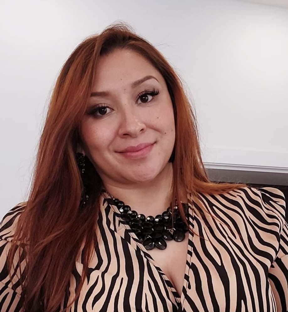Smiling woman with long auburn hair wearing a zebra-print top and chunky black necklace.